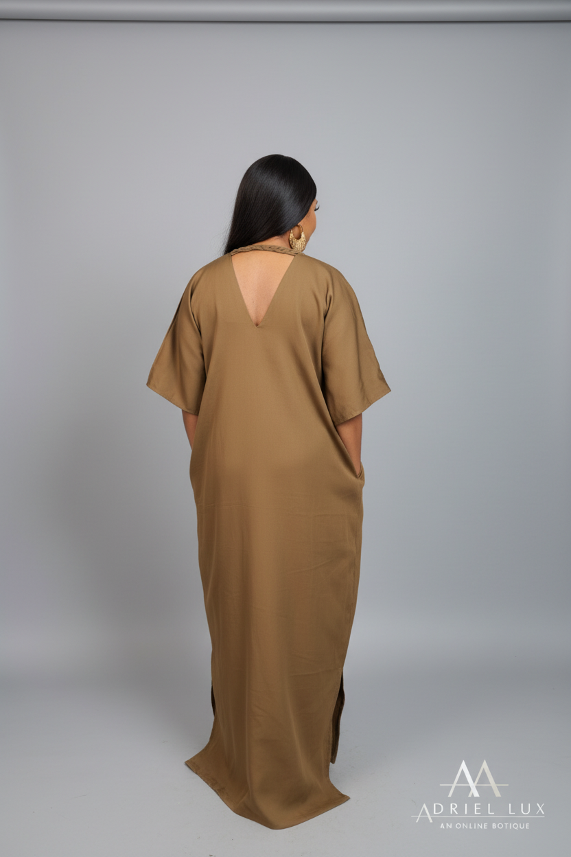 A woman viewed from behind wearing a loose, floor-length khaki dress with a backless open back, standing in a clothing store in front of an Ador Lux banner.